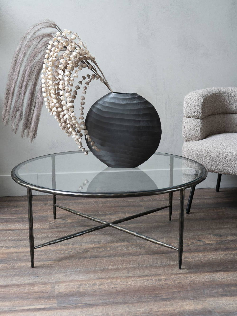 Glass coffee table with a decorative vase and dried plants in a room setting.
