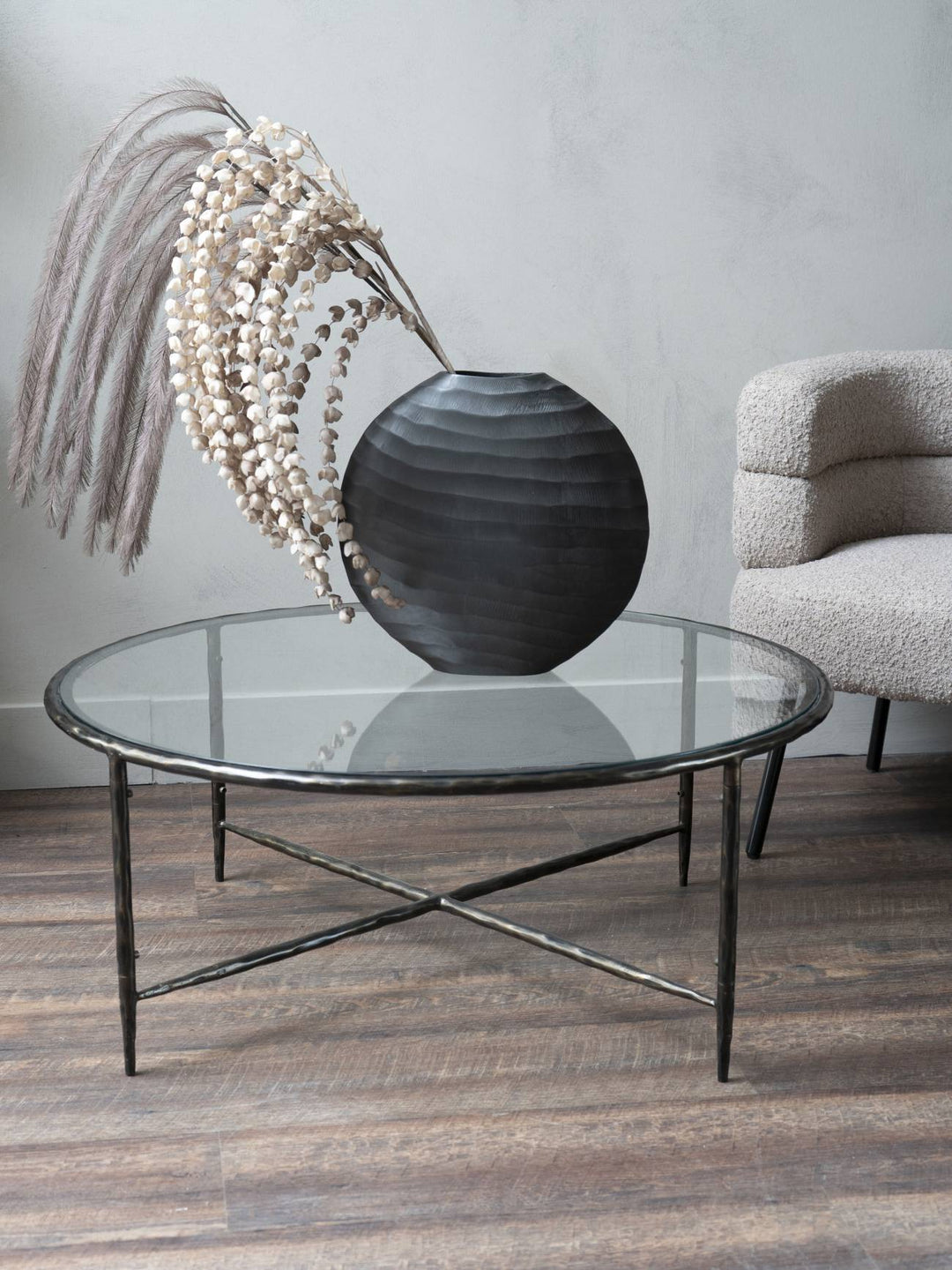 Glass coffee table with a decorative vase and dried plants in a room setting.
