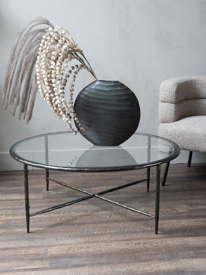 Glass coffee table with a decorative vase and dried plants in a room setting.