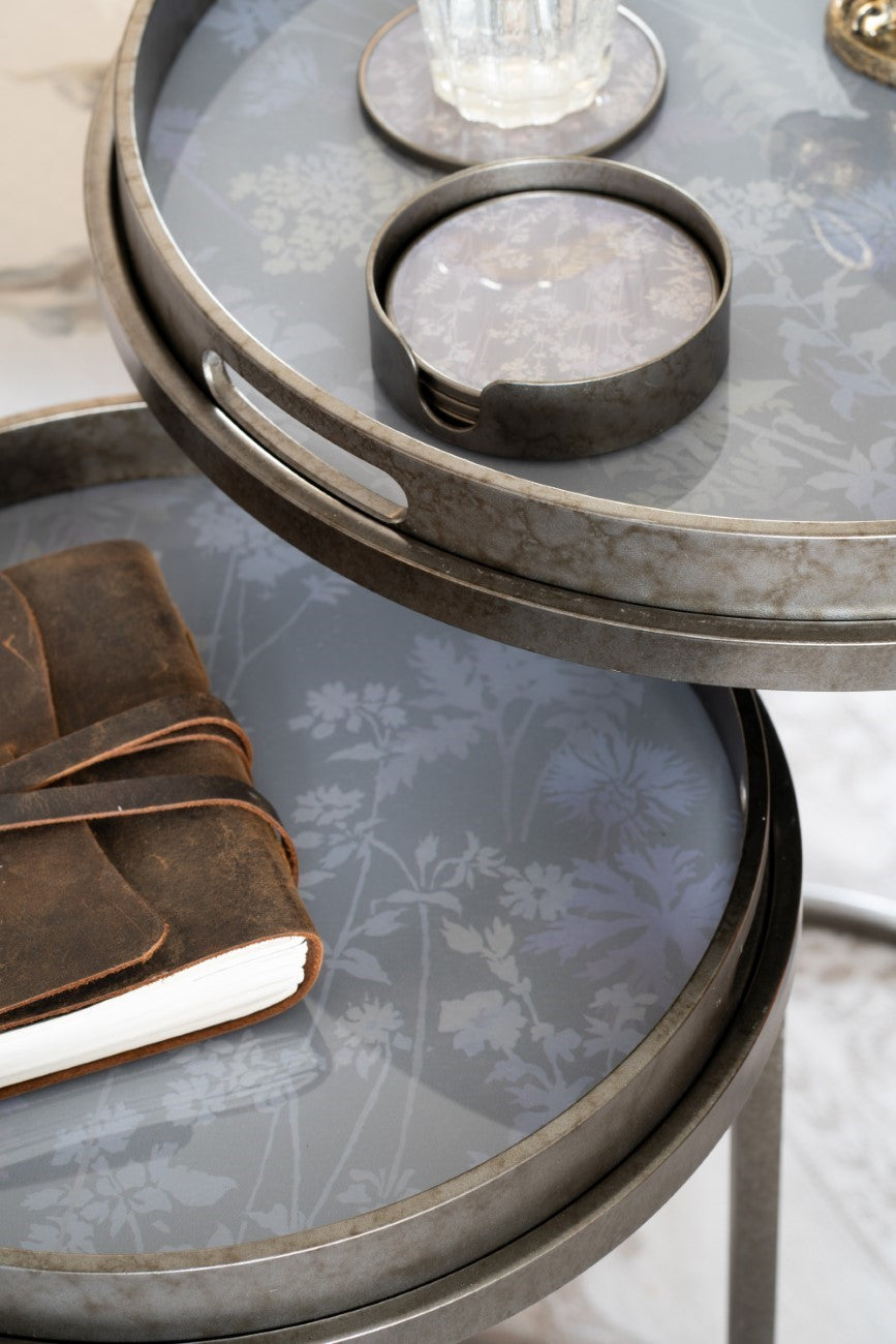 Round glass table with floral pattern and metal base, featuring a leather-bound book.