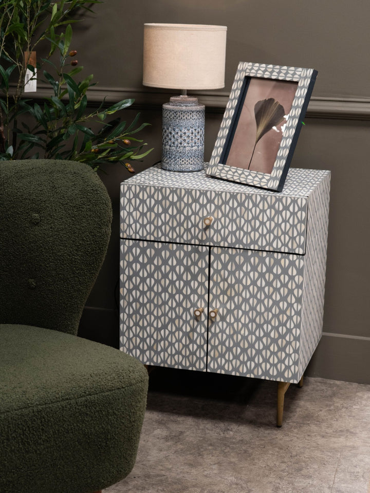 Patterned nightstand with a lamp and photo frame next to a green armchair.