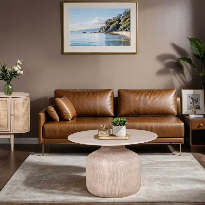Modern living room with brown leather sofa, round coffee table, and framed artwork on wall.