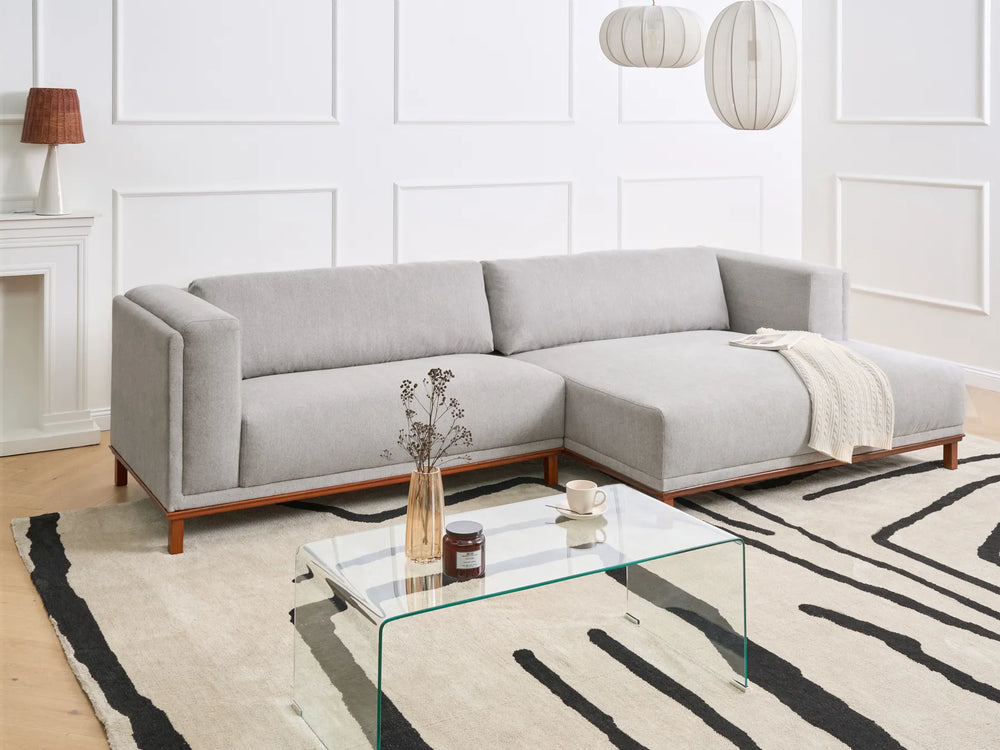 Modern living room with a gray sectional sofa, glass coffee table, and decorative items.