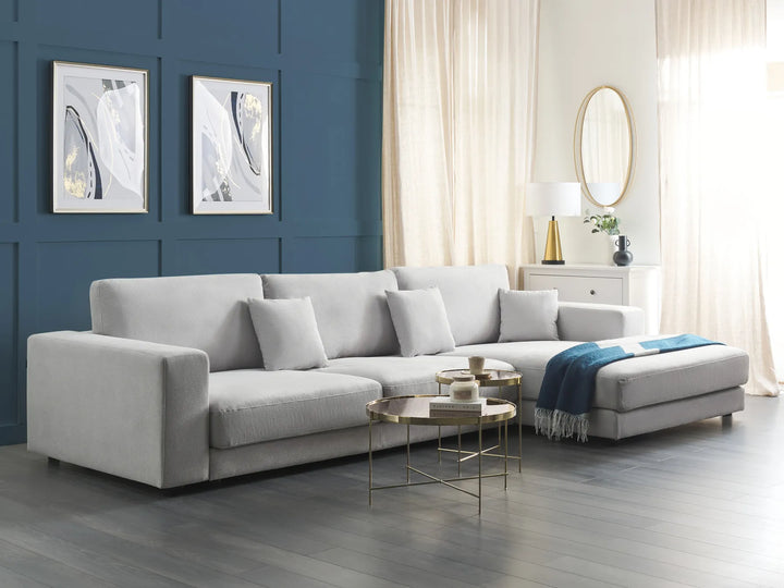 Gray sectional sofa in a living room with blue walls, white curtains, and decorative items.