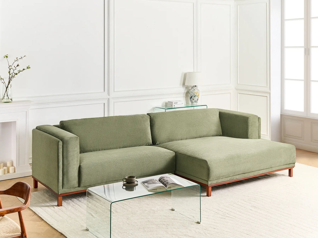 Green sectional sofa in a modern living room with a glass coffee table and decorative items.