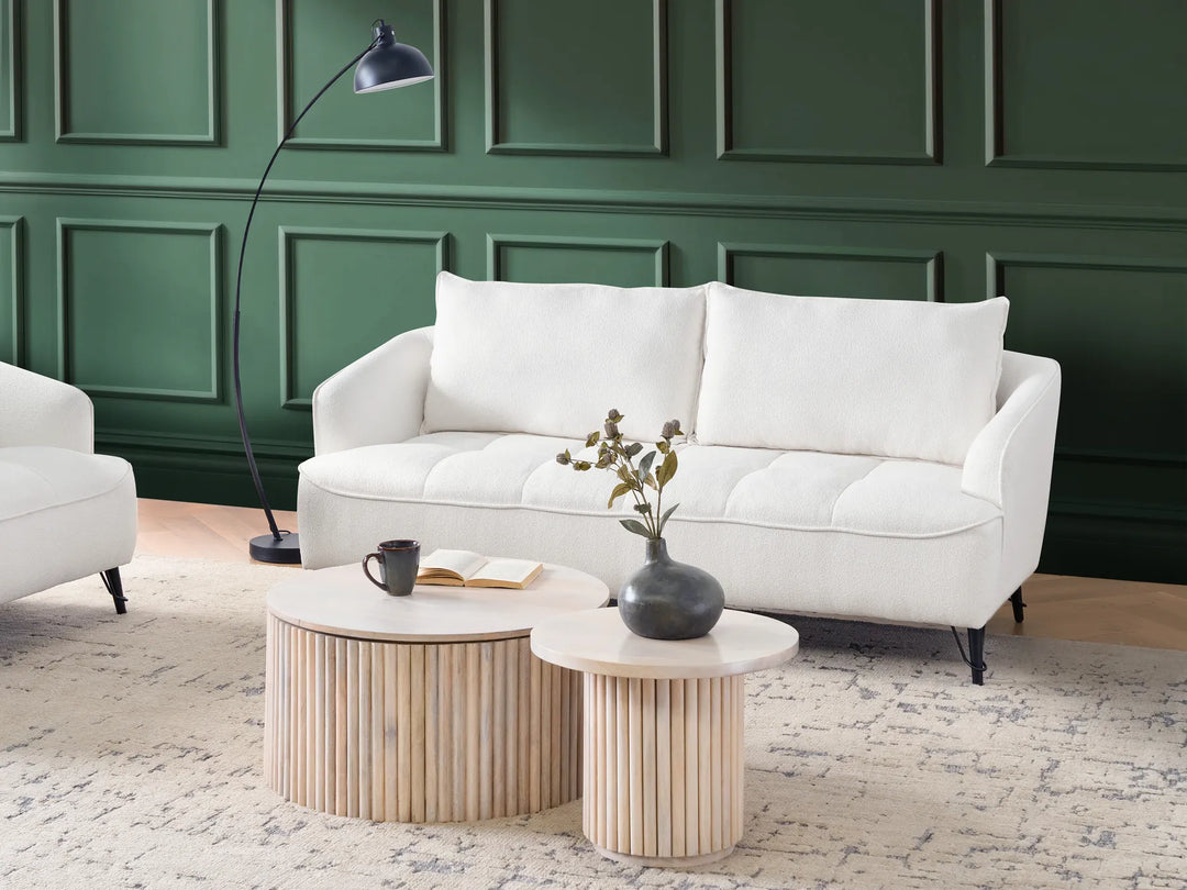 White sofa in a living room with green paneled walls and wooden coffee tables.