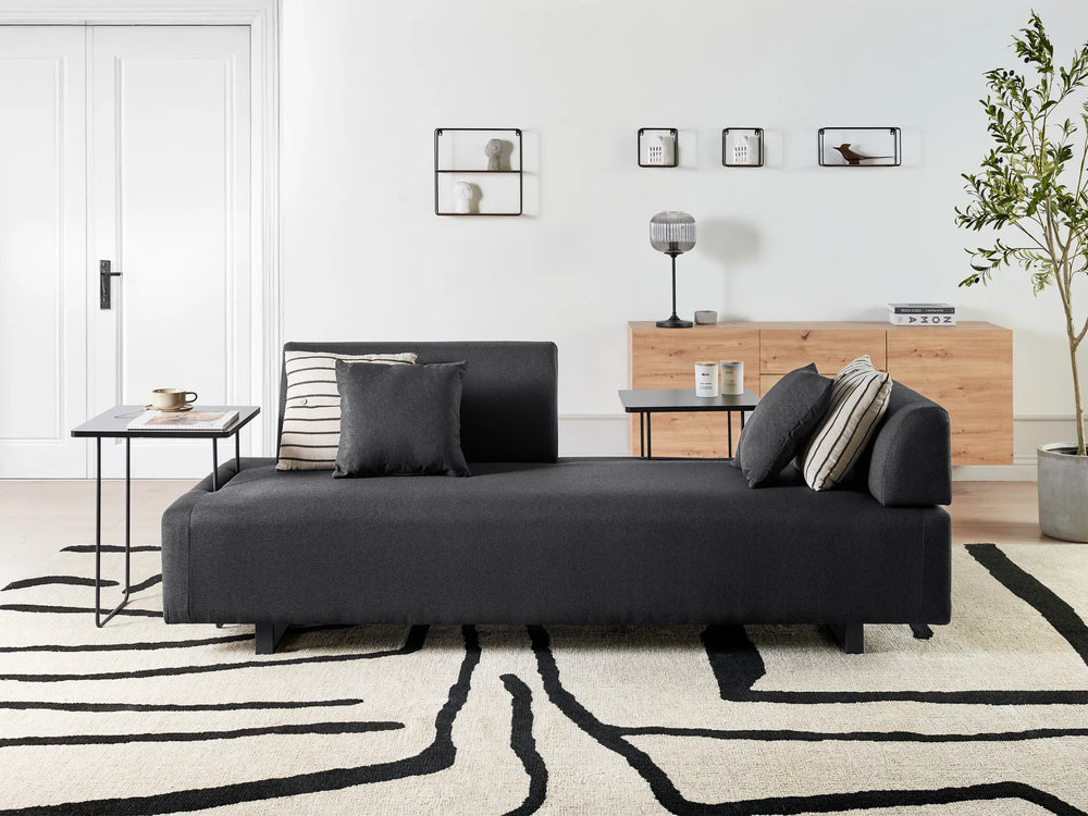 Modern living room with a black sofa, wooden sideboard, and decorative items.