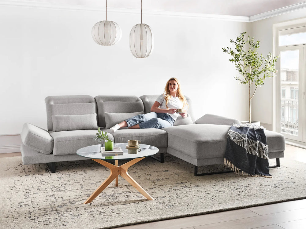 Woman sitting on a gray sectional sofa in a modern living room.