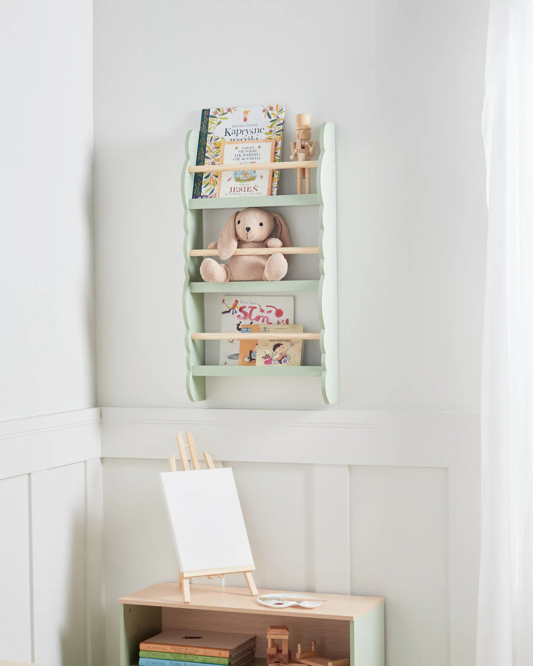 Children's bookshelf with books and a teddy bear against a white wall.