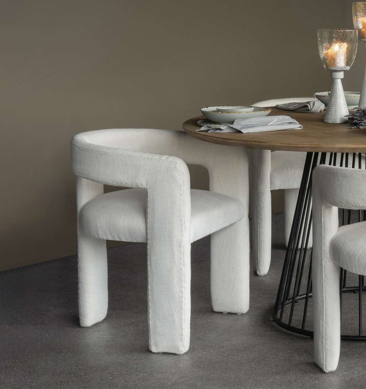 Round wooden dining table with white chairs in a room with a neutral color scheme.