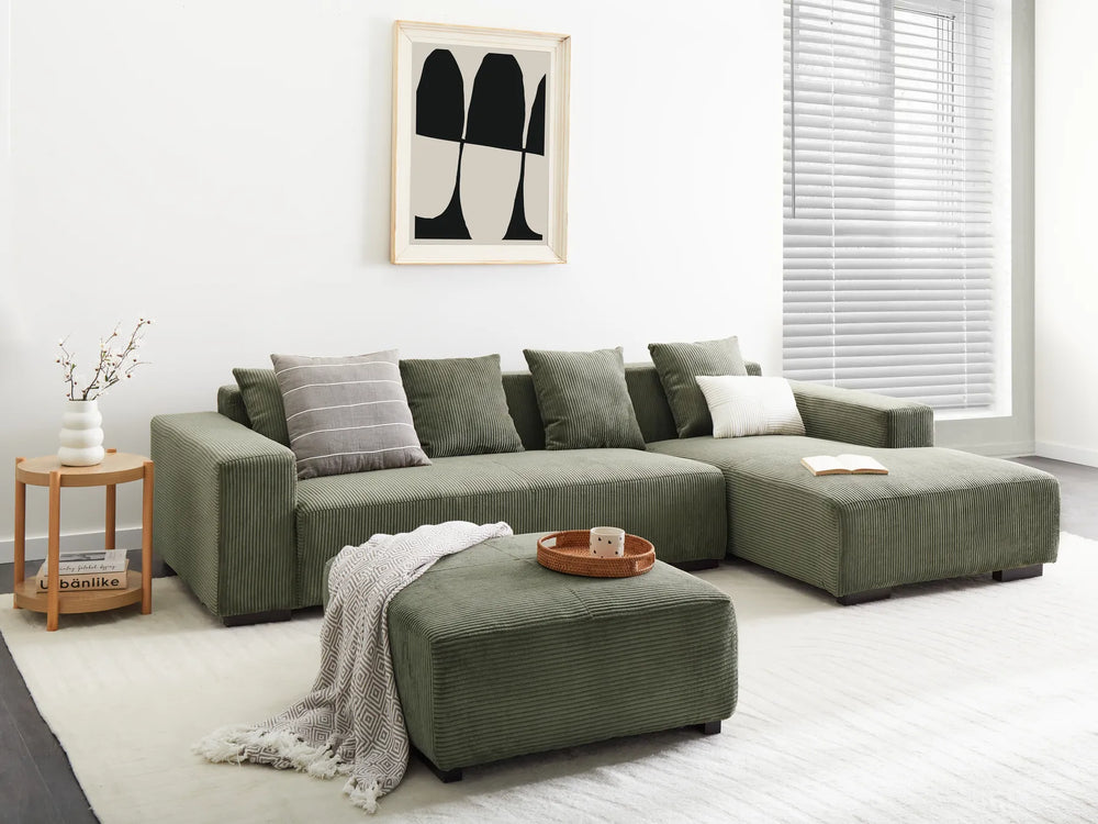 Green sectional sofa in a living room with a side table and abstract art on the wall.