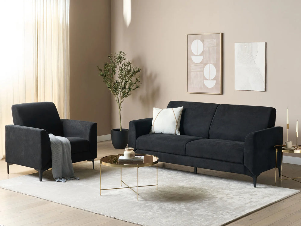 Modern living room with black sofa and armchair, gold coffee table, and decorative elements.