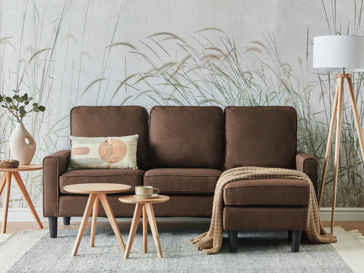 Brown sofa with a decorative pillow and blanket in a room with a textured wall and small tables.