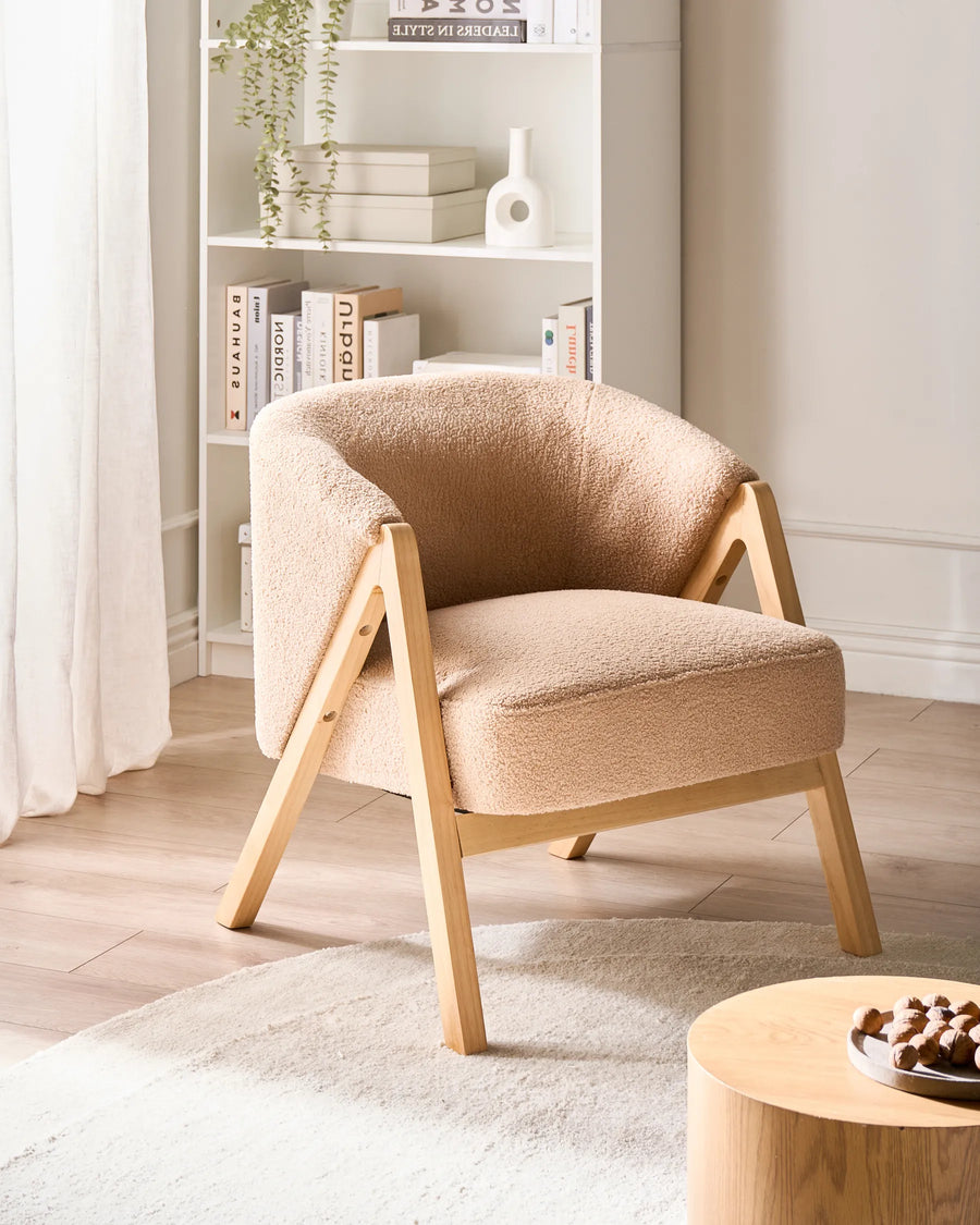Beige armchair in a room with a bookshelf and small table.