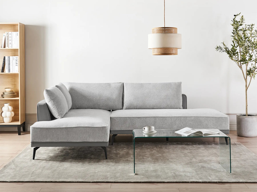 Gray sectional sofa in a living room with a glass coffee table, bookshelf, and plant.