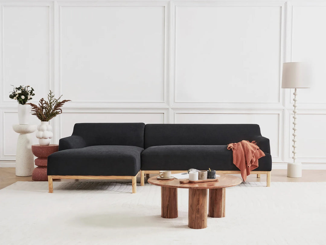 Black sectional sofa in a modern living room with a wooden coffee table and decorative items.