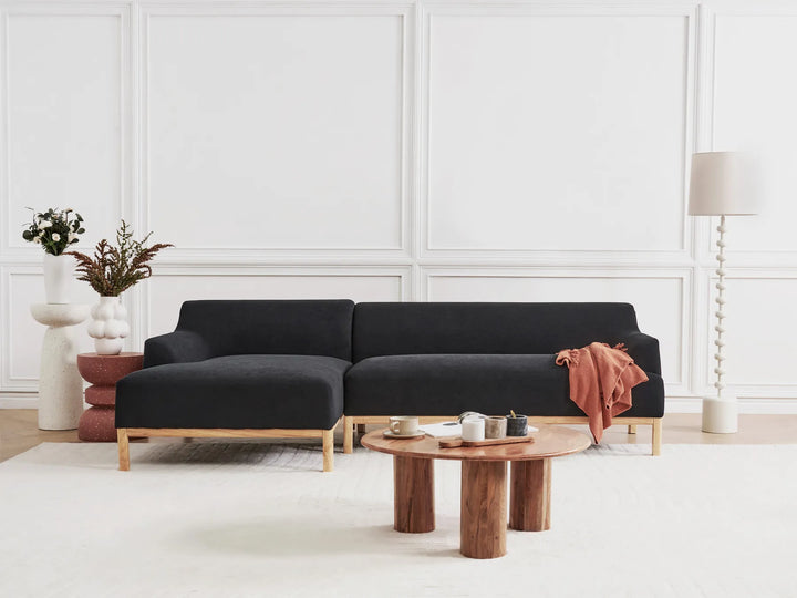 Black sectional sofa in a modern living room with a wooden coffee table and decorative items.