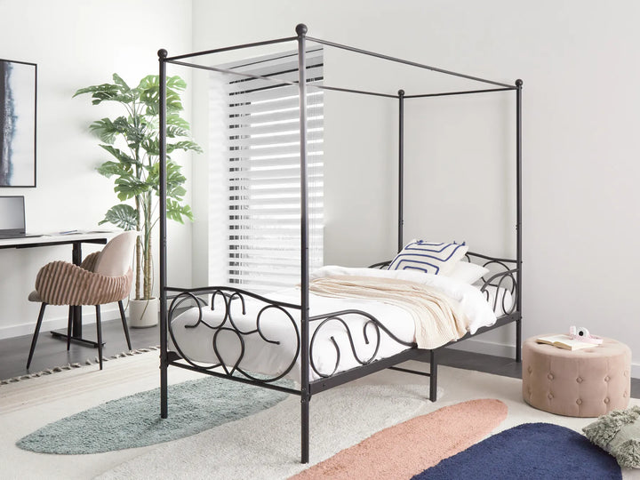 Black metal canopy bed in a room with a desk and plant