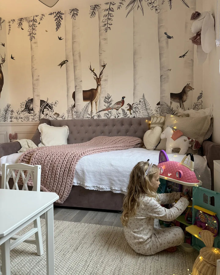 Child playing with toys in a bedroom with forest-themed wallpaper