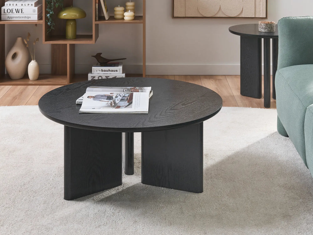 Round black coffee table in a living room setting with a book and magazine on top.