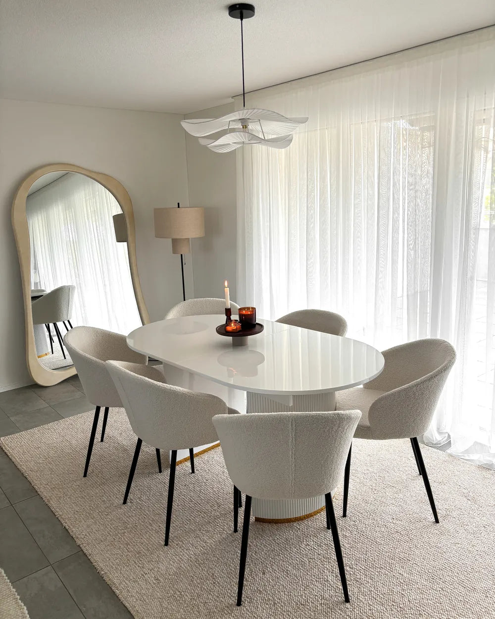 Modern dining room with a white oval table and chairs, large mirror, and decorative elements.