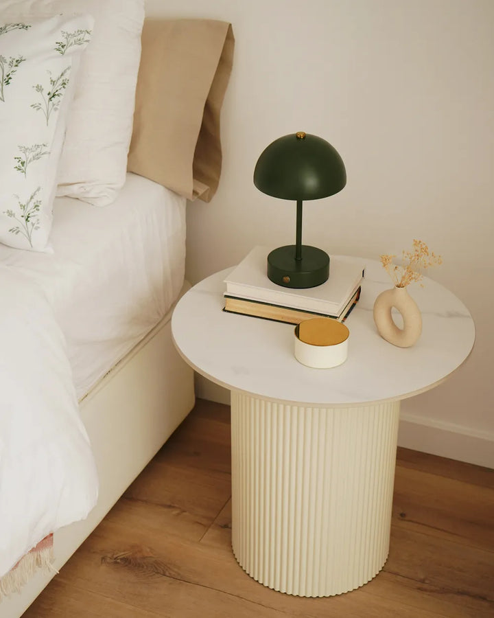 Round side table with decorative items next to a bed