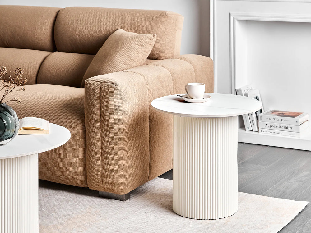 Beige sofa with a white side table and decorative items in a living room setting.