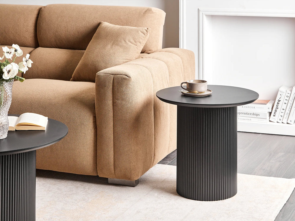Beige sofa with a black side table and decorative items in a living room setting.
