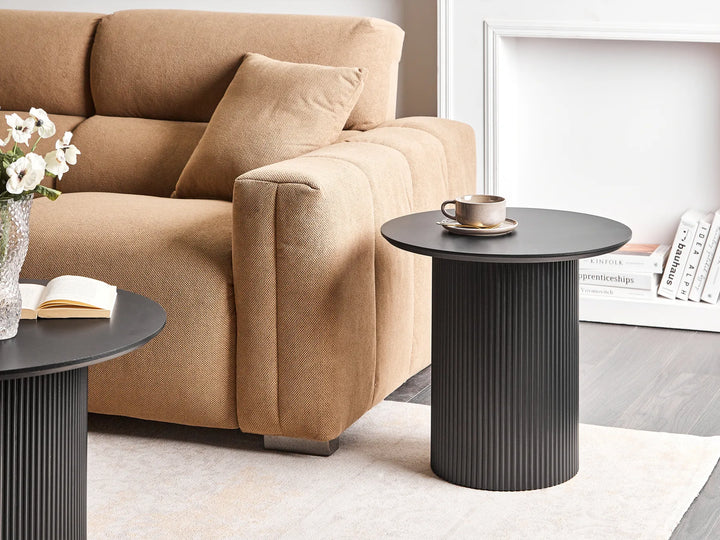Beige sofa with a black side table and decorative items in a living room setting.