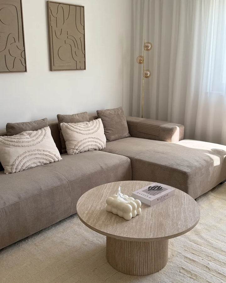 Modern living room with a beige sectional sofa and round wooden coffee table.