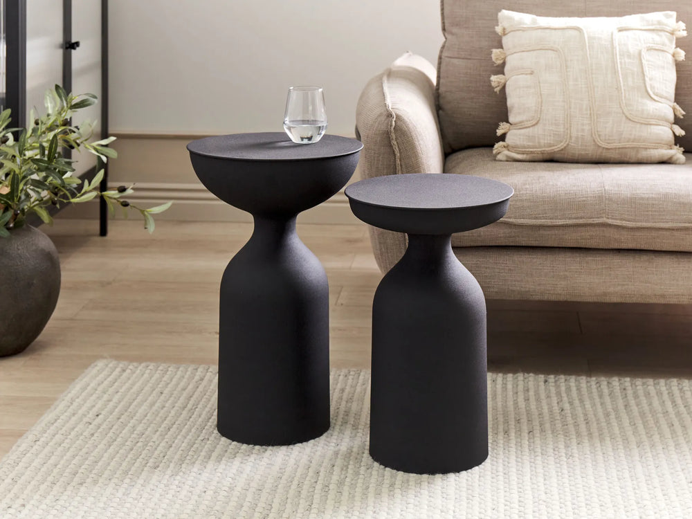 Two black side tables in a living room setting with a couch and plant.