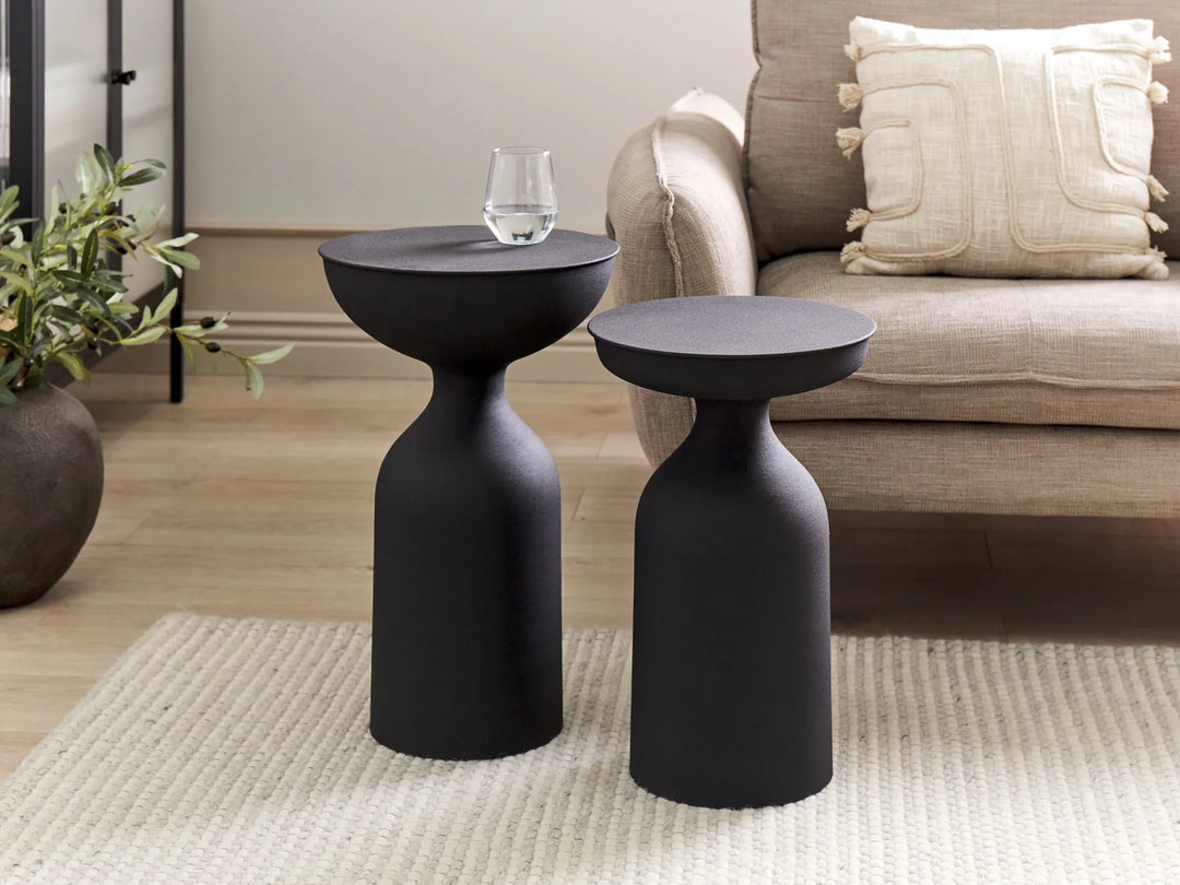 Two black side tables in a living room setting with a couch and plant.