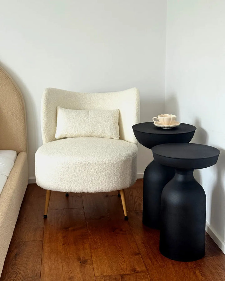 White armchair with a beige pillow next to black side tables on a wooden floor.