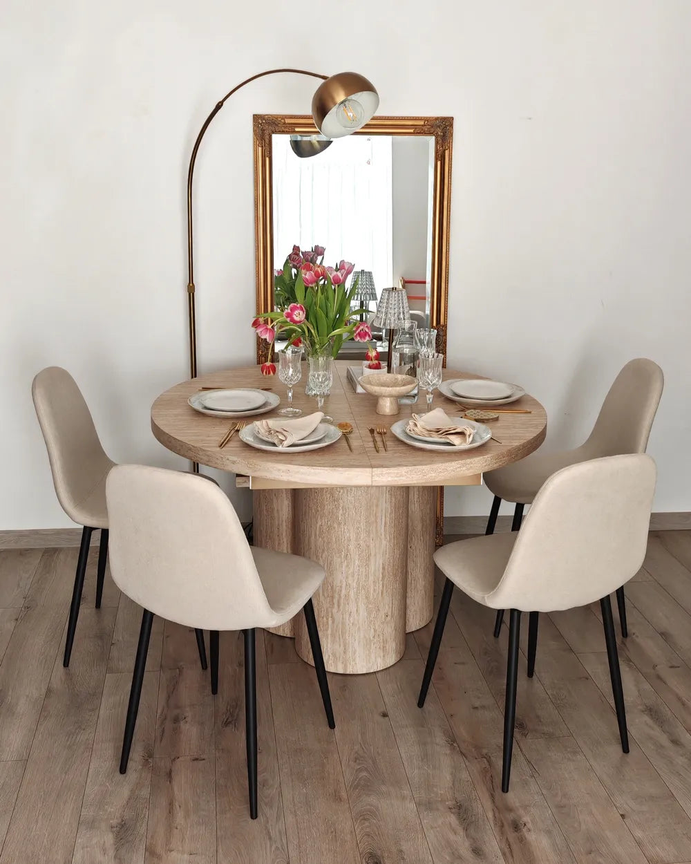 Dining room with a round wooden table and four beige chairs, set for a meal.