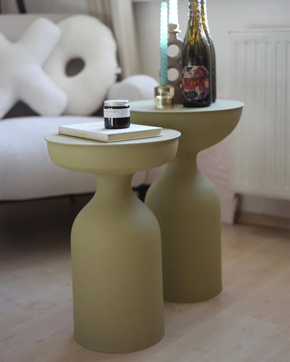 Two green side tables with a bottle and books on a light wood floor.