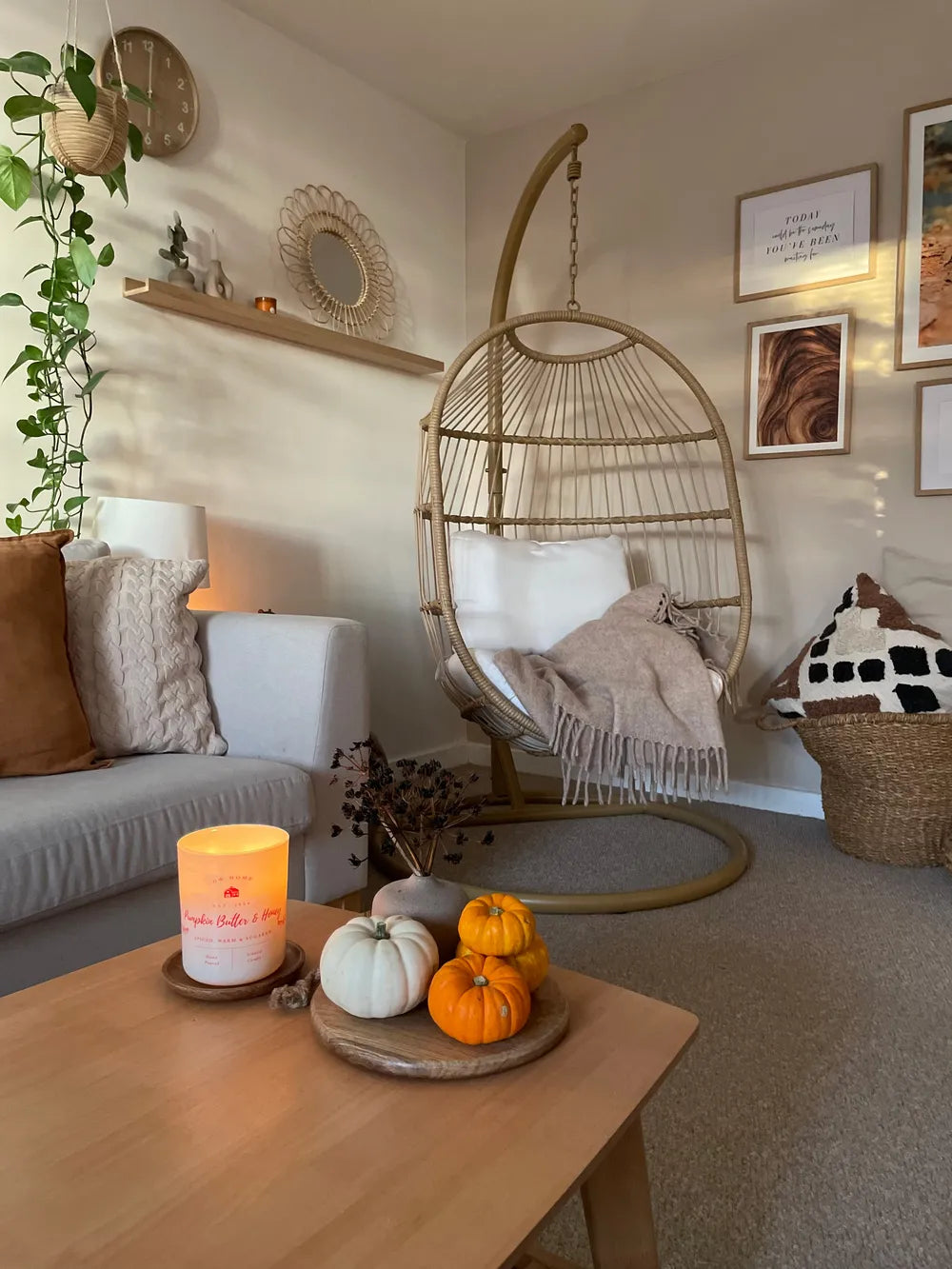 Cozy living room with a hanging chair, candles, and pumpkins on a table.