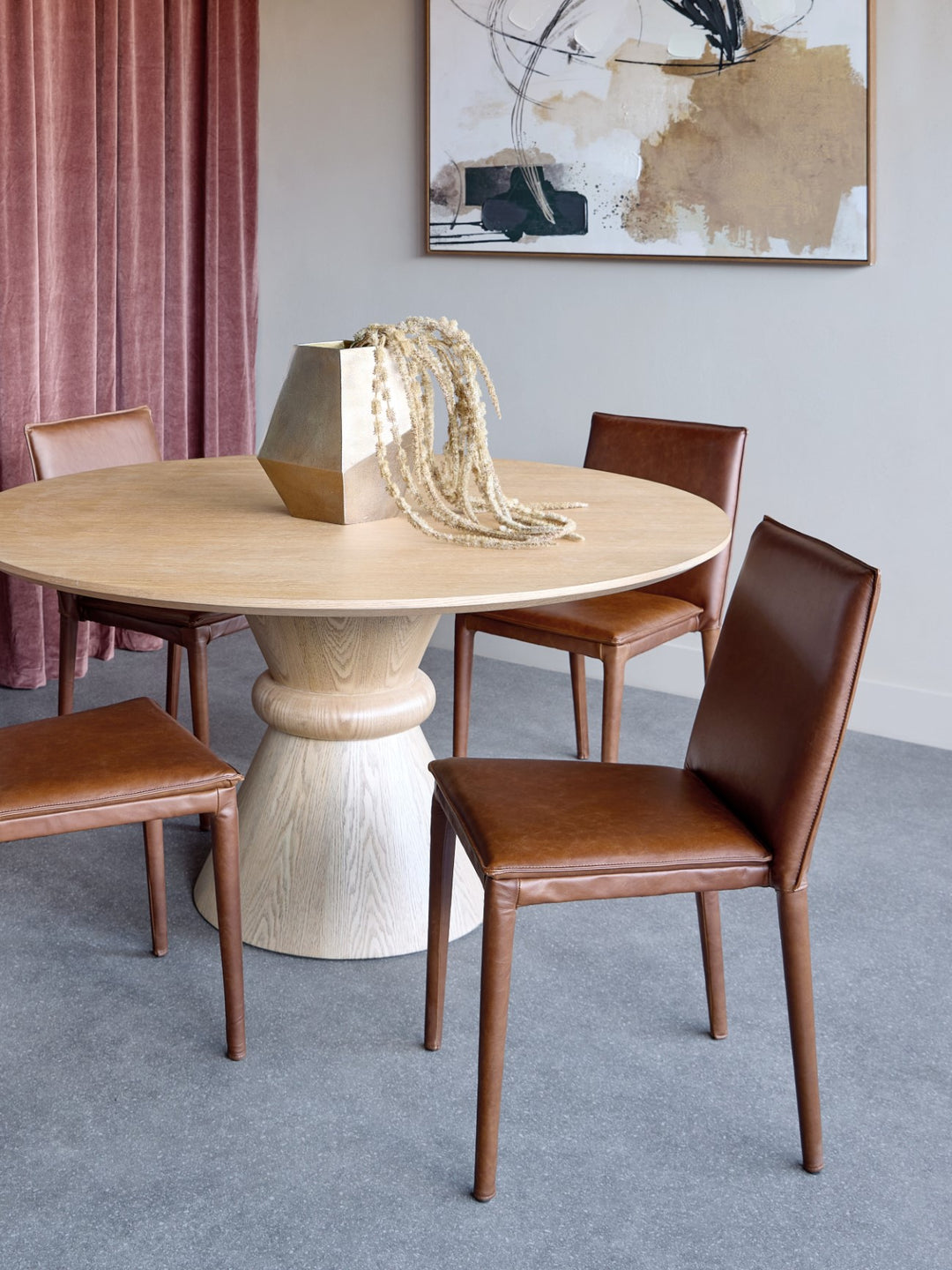 Dining room with a round wooden table and brown chairs, featuring abstract art on the wall.
