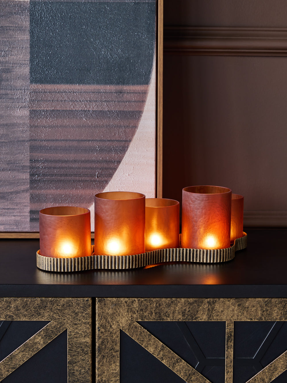 Set of lit candles in decorative holders on a dark surface with a textured wall in the background