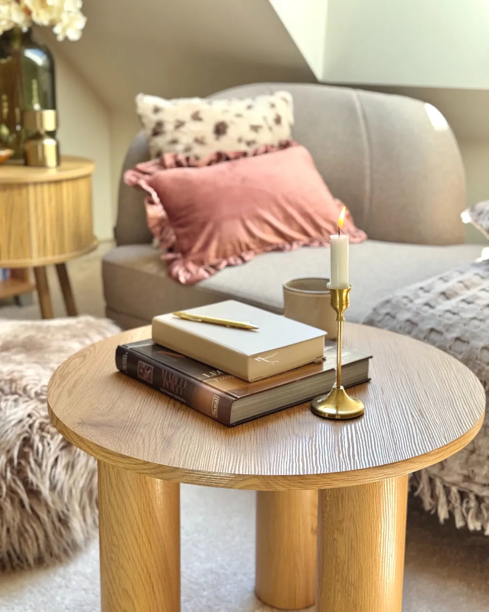 Round wooden coffee table with books, a candle, and a pen in a cozy living room setting.