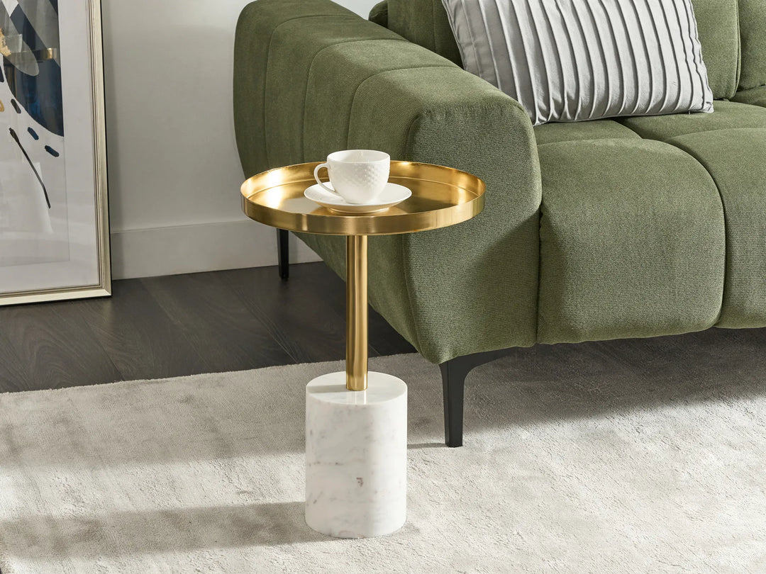 Gold side table with a white cup and saucer next to a green sofa.