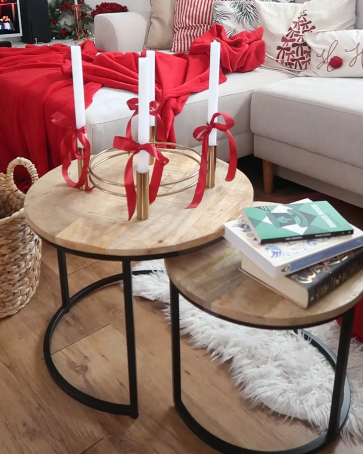 Round wooden coffee table with candles and red ribbons in a living room setting.