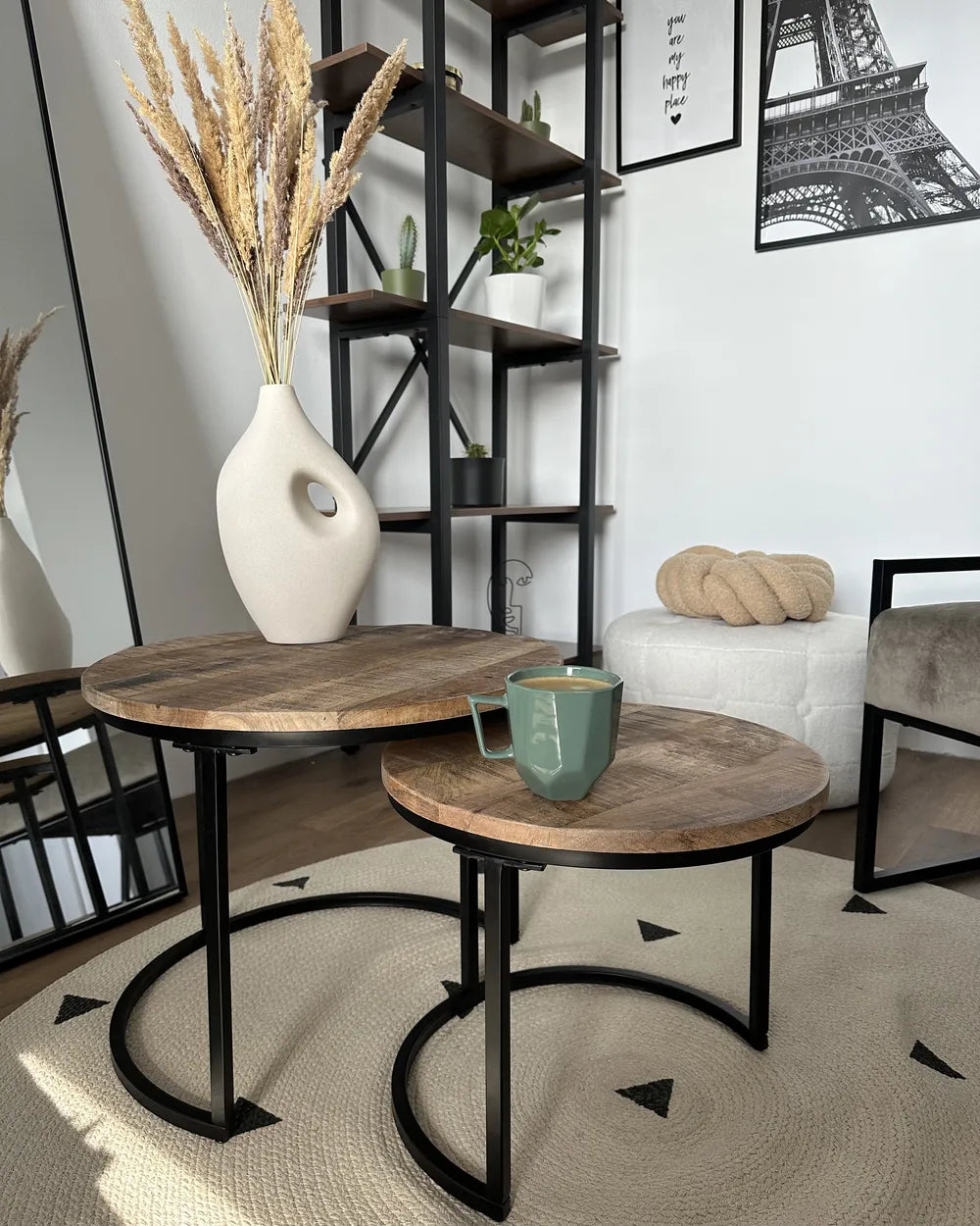 Two wooden tables with black metal legs in a room with a shelf and decorative items.