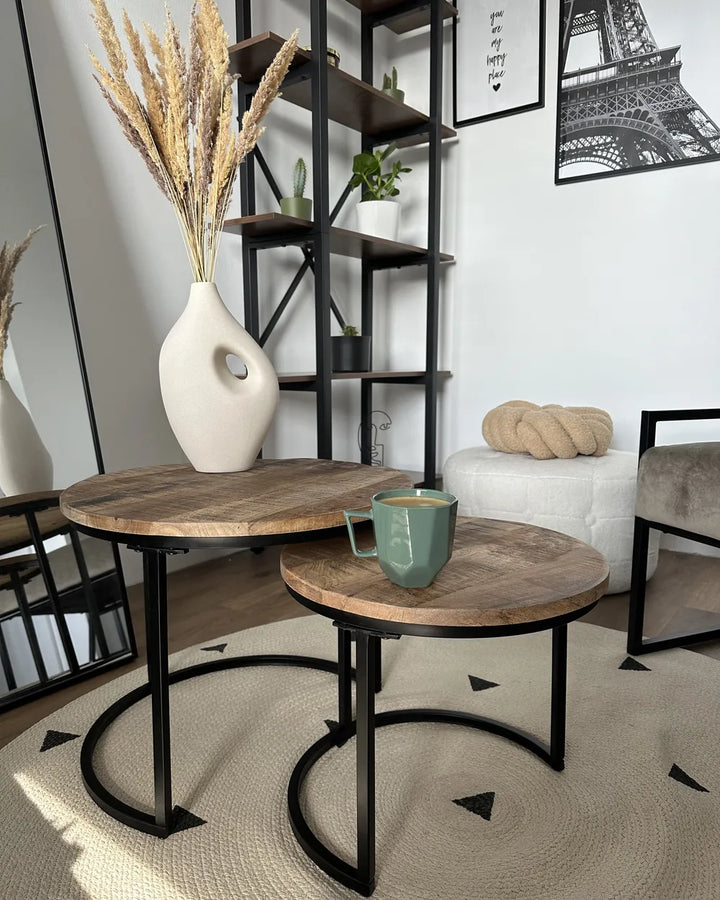 Two wooden tables with black metal legs in a room with a shelf and decorative items.