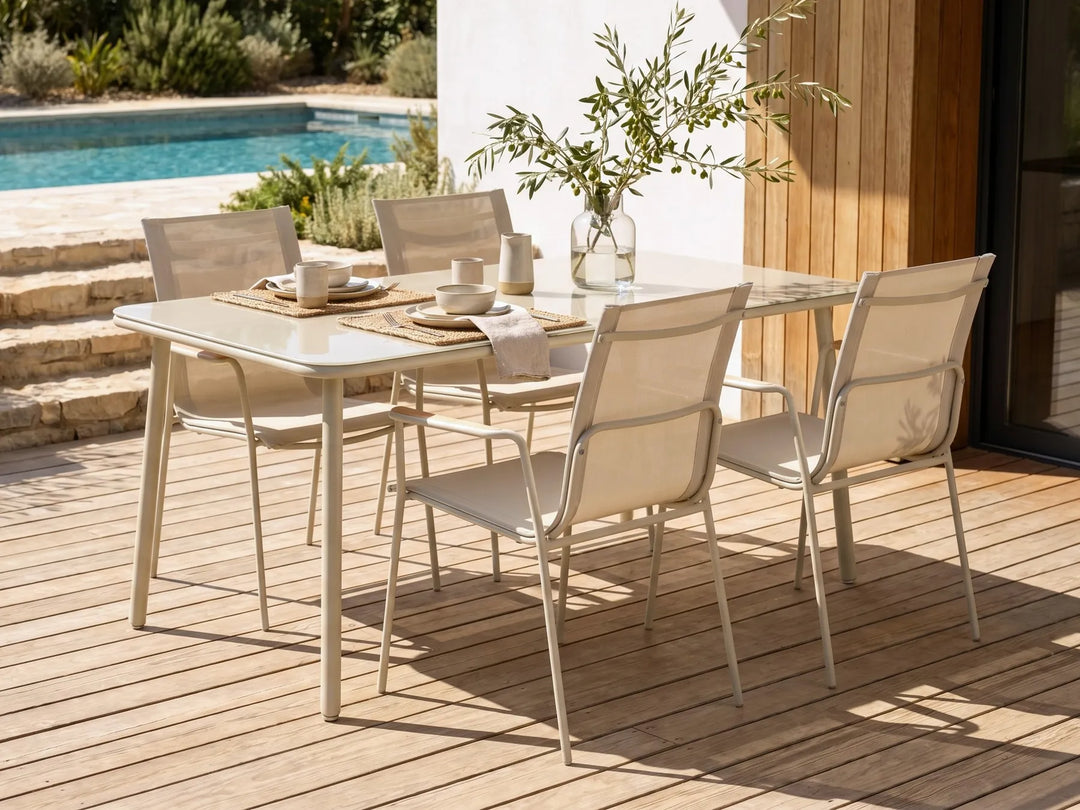 Outdoor dining set with table and chairs on a wooden deck near a pool.