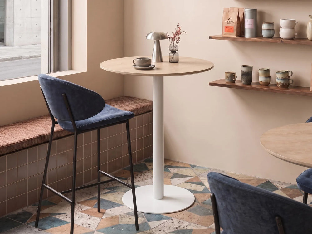 Small cafe interior with a round table and chairs near a window.