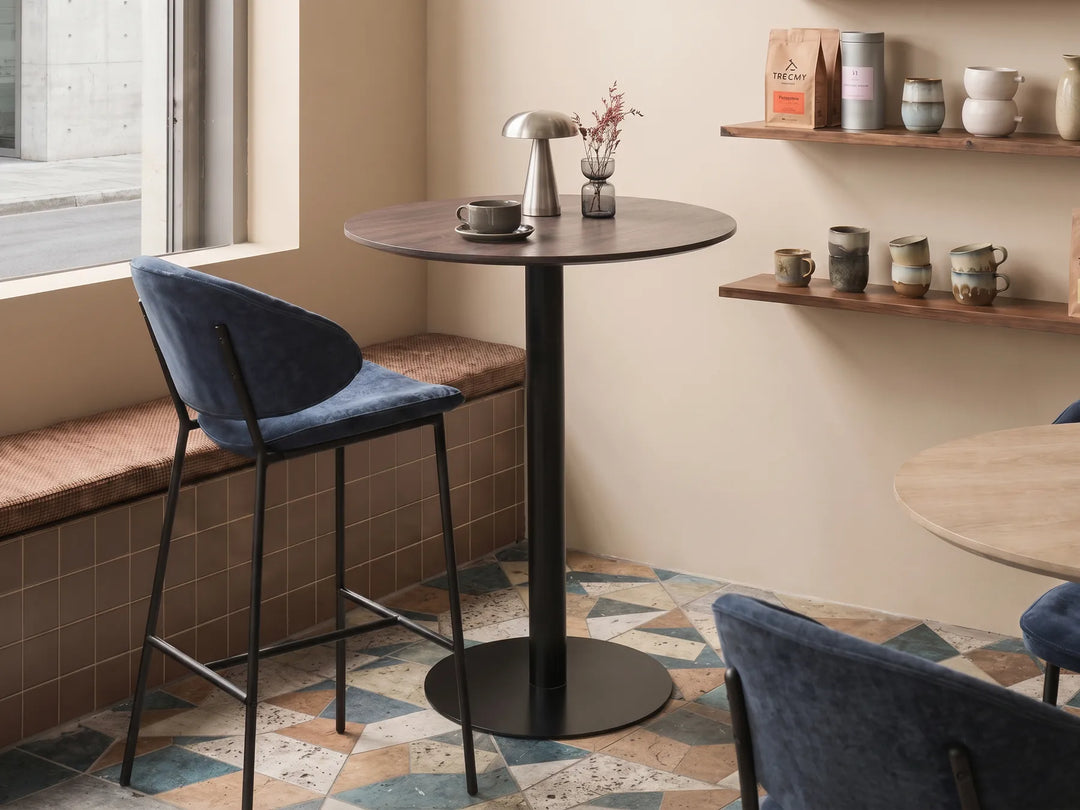 Modern interior with a round black table and blue chairs in a room with a window and shelves.
