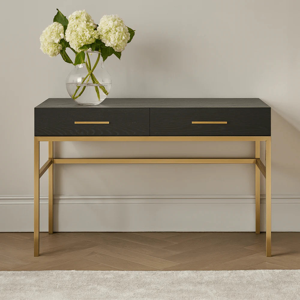 Console table with black top and gold legs against a neutral wall.
