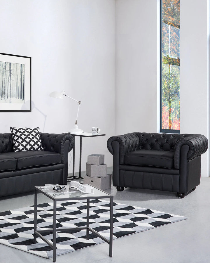 Modern living room with black Chesterfield sofas, a glass coffee table, and decorative items.