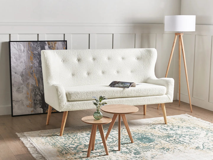 White tufted sofa in a living room with wooden side tables and a lamp.