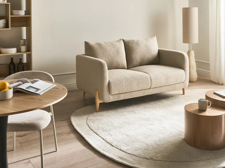 Modern living room with a beige sofa, round rug, and wooden furniture.